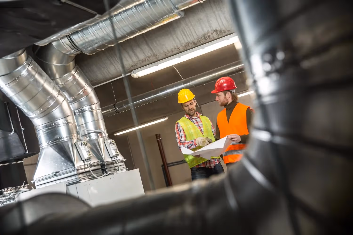Workers check plans near HVAC ducts.