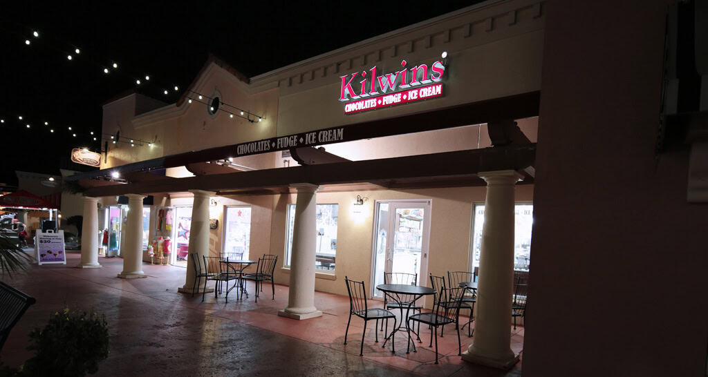 Illuminated Kilwins storefront and sidewalk seating at night in Myrtle Beach, SC.