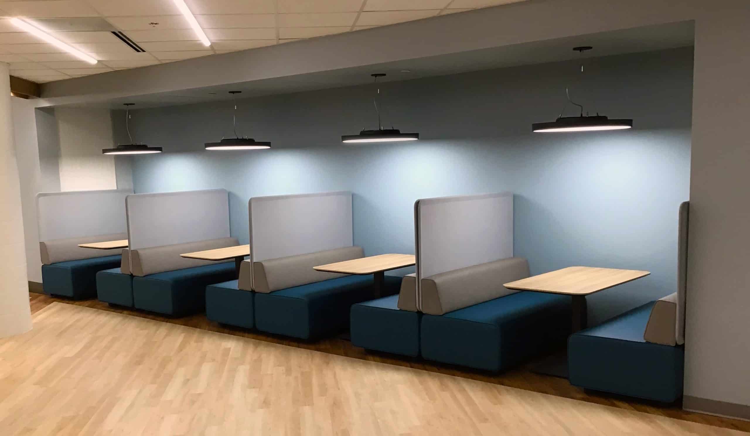 Row of navy booths with wood tables under pendant lights in the renovated Grand Cafe at Grand Strand Regional Medical Center.