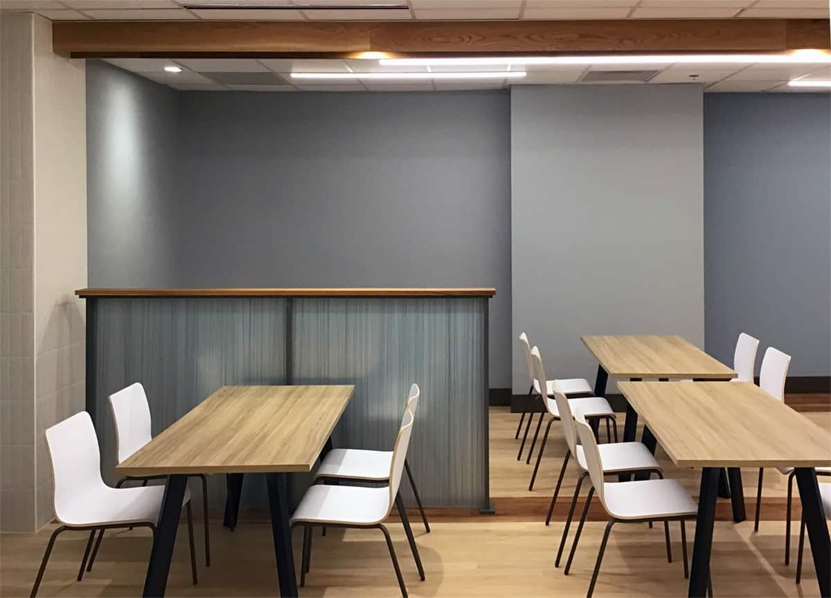 Tables and chairs in front of a wood-topped half-wall partition in the renovated cafeteria.