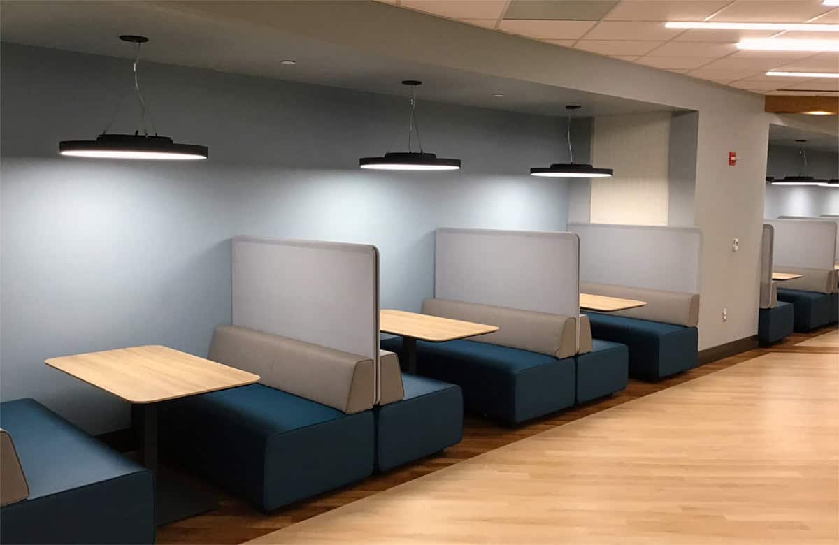 Upholstered booths with wood tabletops and pendant lighting along a light blue wall.