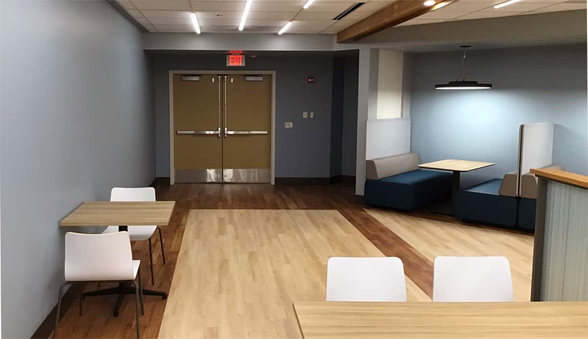 Cafeteria seating with tables and booths, with double doors on the far wall.