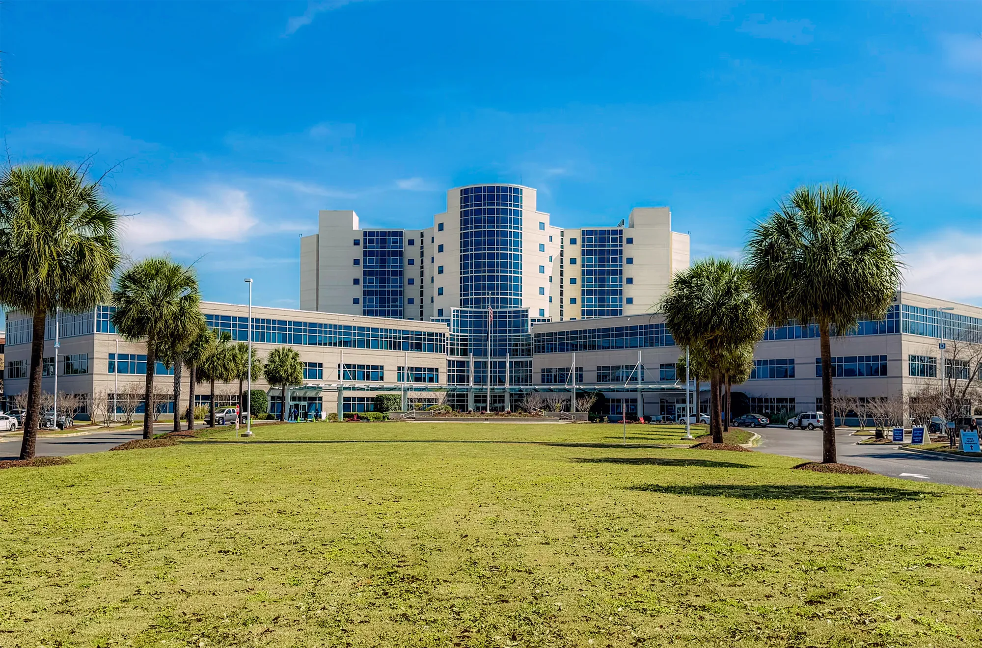 Wide front view of MUSC Florence Medical Center beyond its lawn and palm trees.