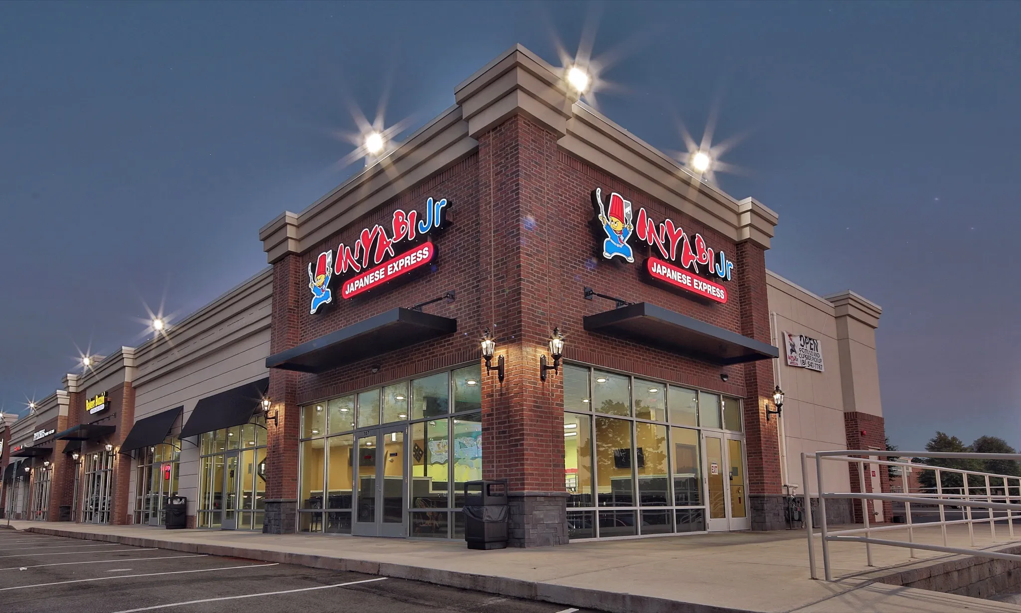 Wide dusk view of Miyabi Jr.'s glass storefront and entrance ramp in Tega Cay.