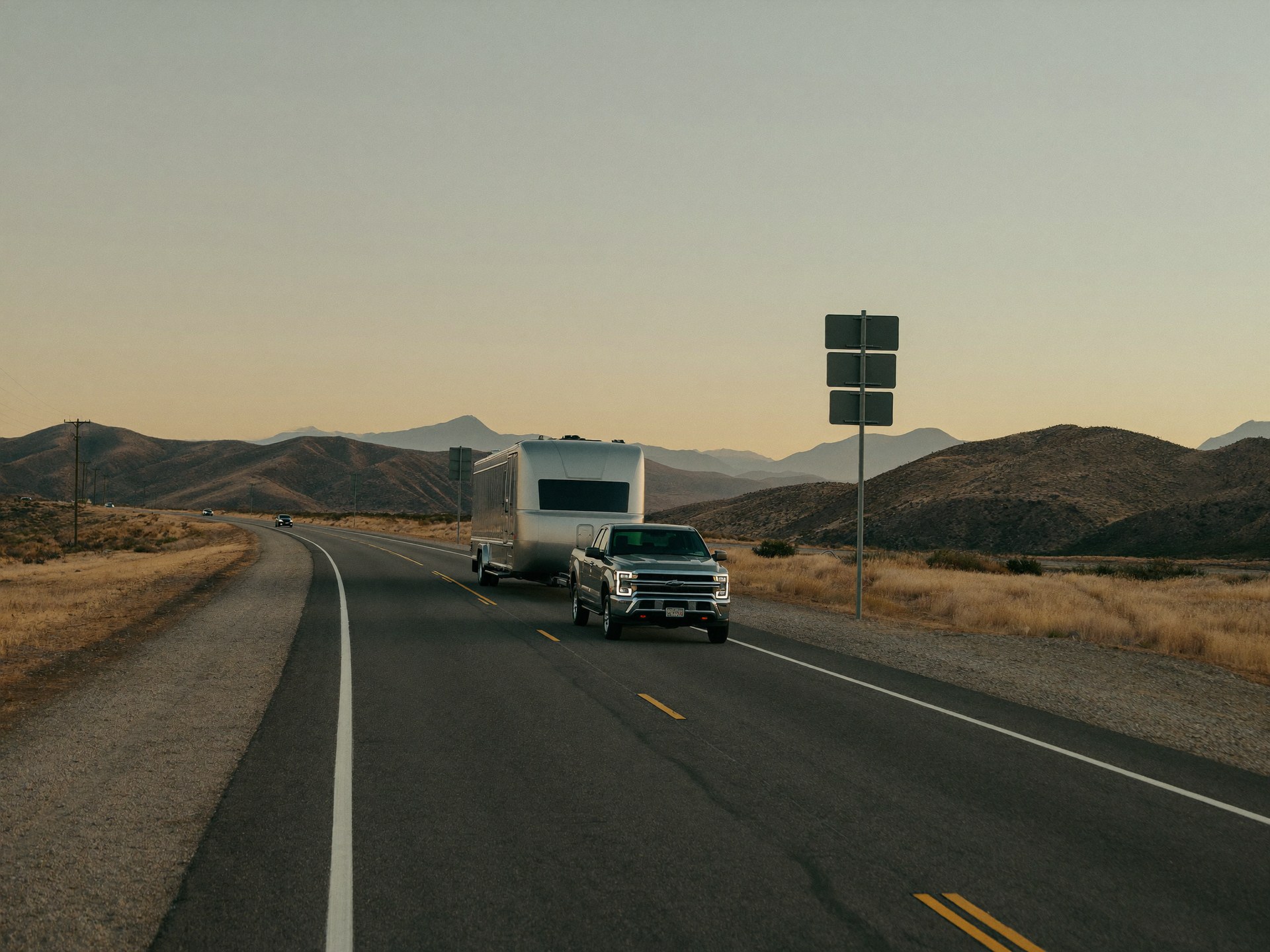 Truck towing a trailer on an open highway at golden hour
