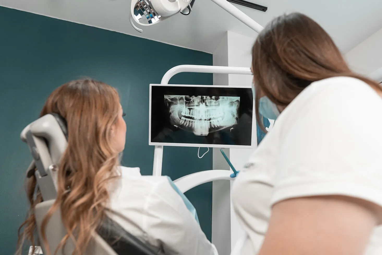 A patient sitting in a dental chair while a dentist reviews and explains a digital dental X-ray on a screen during a consultation.