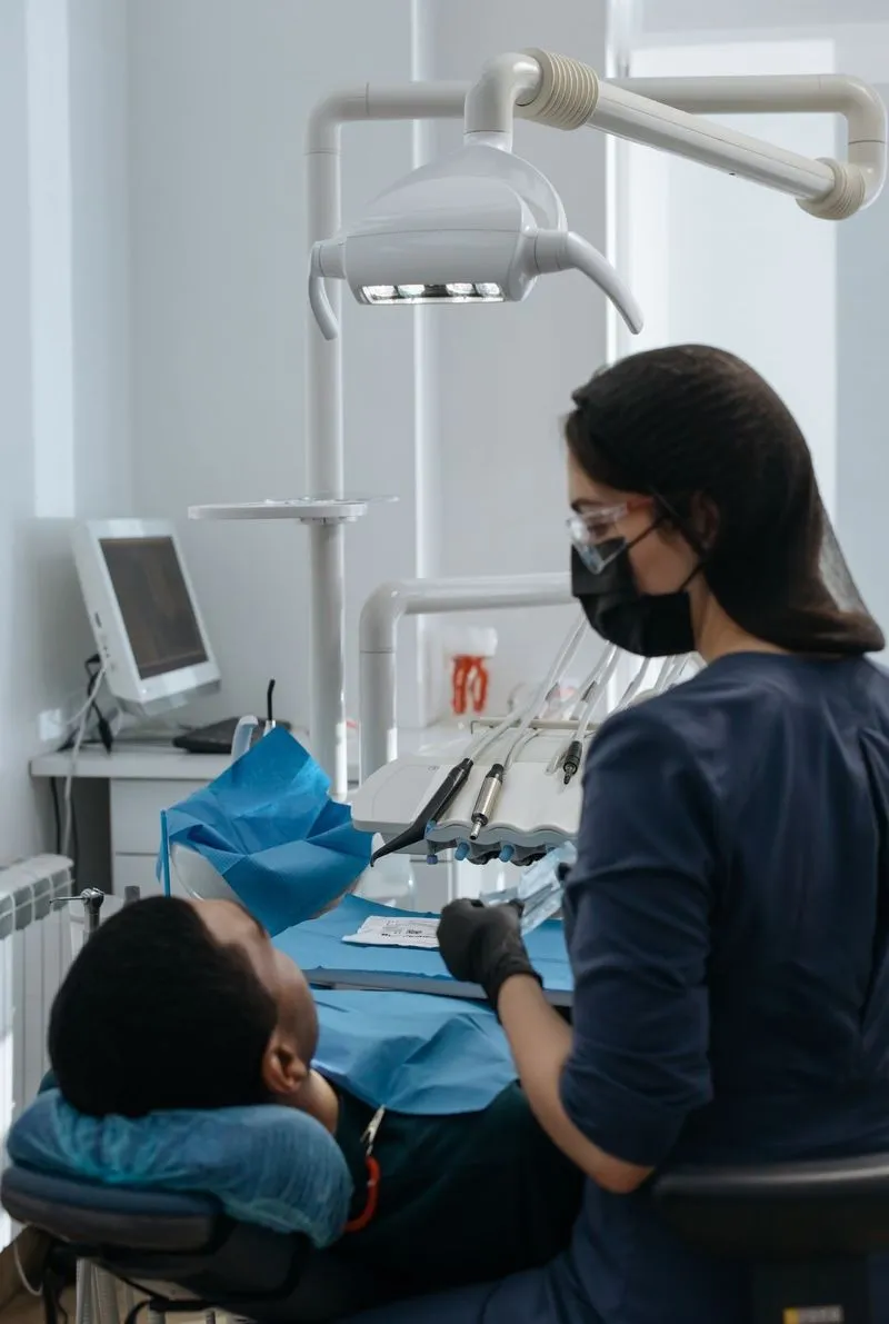 A dentist performing treatment on a patient using a blue rubber dam for tooth isolation in a modern dental operatory.
