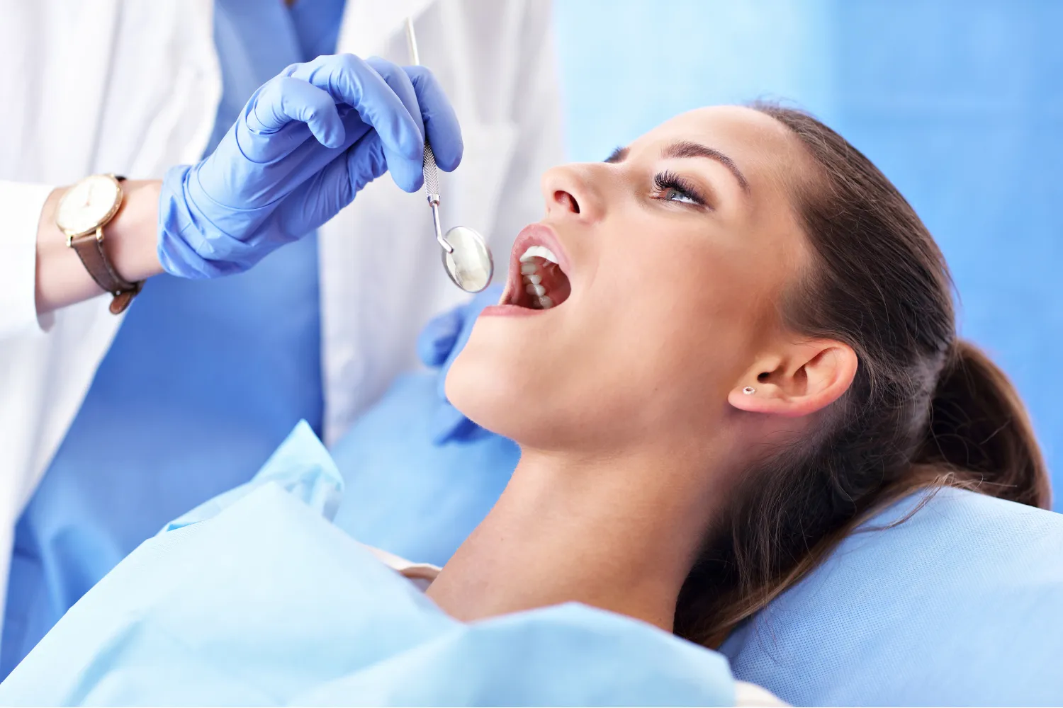 A female patient reclined in a dental chair with her mouth open as a dentist prepares to fit a clear aligner over her teeth.