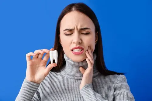 A woman grimacing in pain while touching her cheek, holding a dental model with an extracted tooth, symbolizing dental discomfort or surgery.