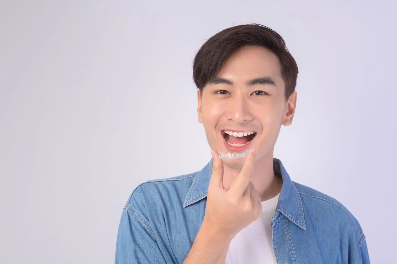 A young man smiling and pointing to his teeth, showcasing confidence and satisfaction with dental or orthodontic care results.