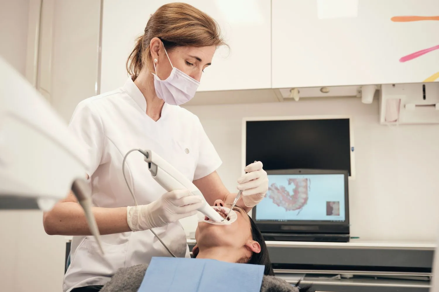 A female dentist in a white coat and gloves performing a dental procedure on a patient in a well-equipped clinic.