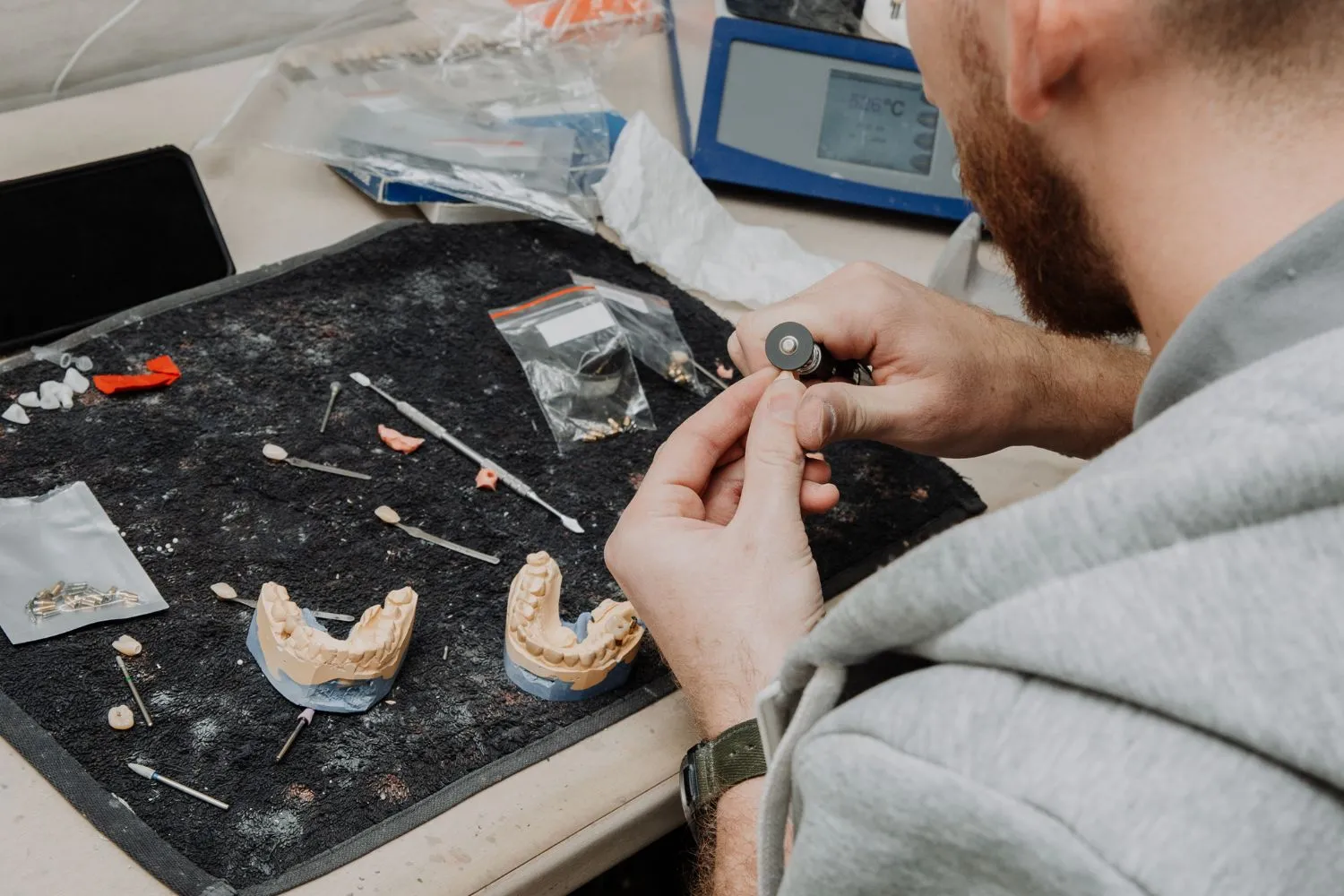 A dental technician working at a lab bench with tools and molds, meticulously crafting crowns or bridges on dental models.