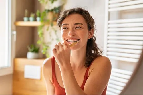 A smiling woman practicing good oral hygiene by flossing her teeth in a cozy home bathroom environment.