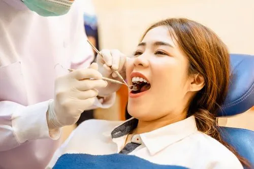 A woman sitting in a dental chair with her mouth open as a dentist examines her teeth using a dental mirror and explorer.