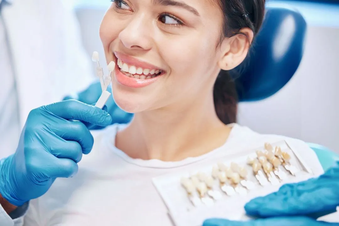 A cheerful young woman in the dental chair during a shade matching session with a dentist using a tooth color guide.