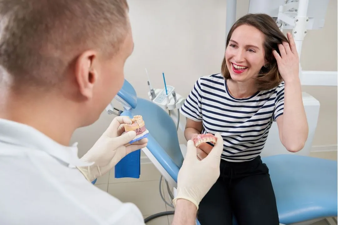 A smiling female dental patient consults with a dentist during a teeth shade matching session in a modern dental clinic.