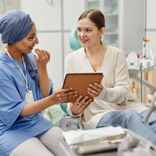 A healthcare professional and patient smiling while reviewing dental information together on a tablet in a clinical setting.