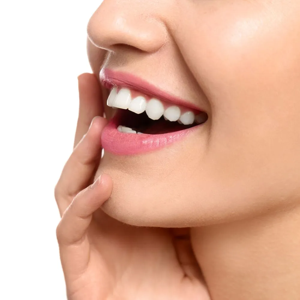 Close-up side profile of a woman’s bright white smile with smooth pink lips and hand gently resting on her cheek.