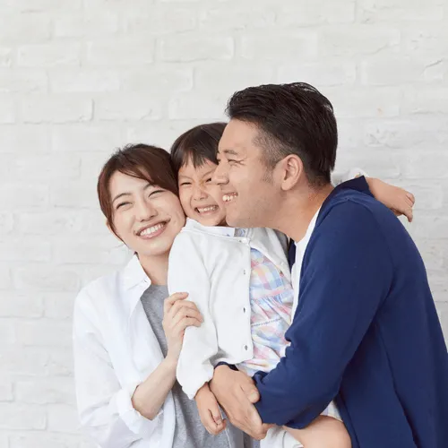 An Asian family of three smiling warmly in front of a white brick wall, radiating love and togetherness.