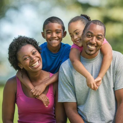 A cheerful African American family of four smiling outdoors, showcasing happiness and unity.

