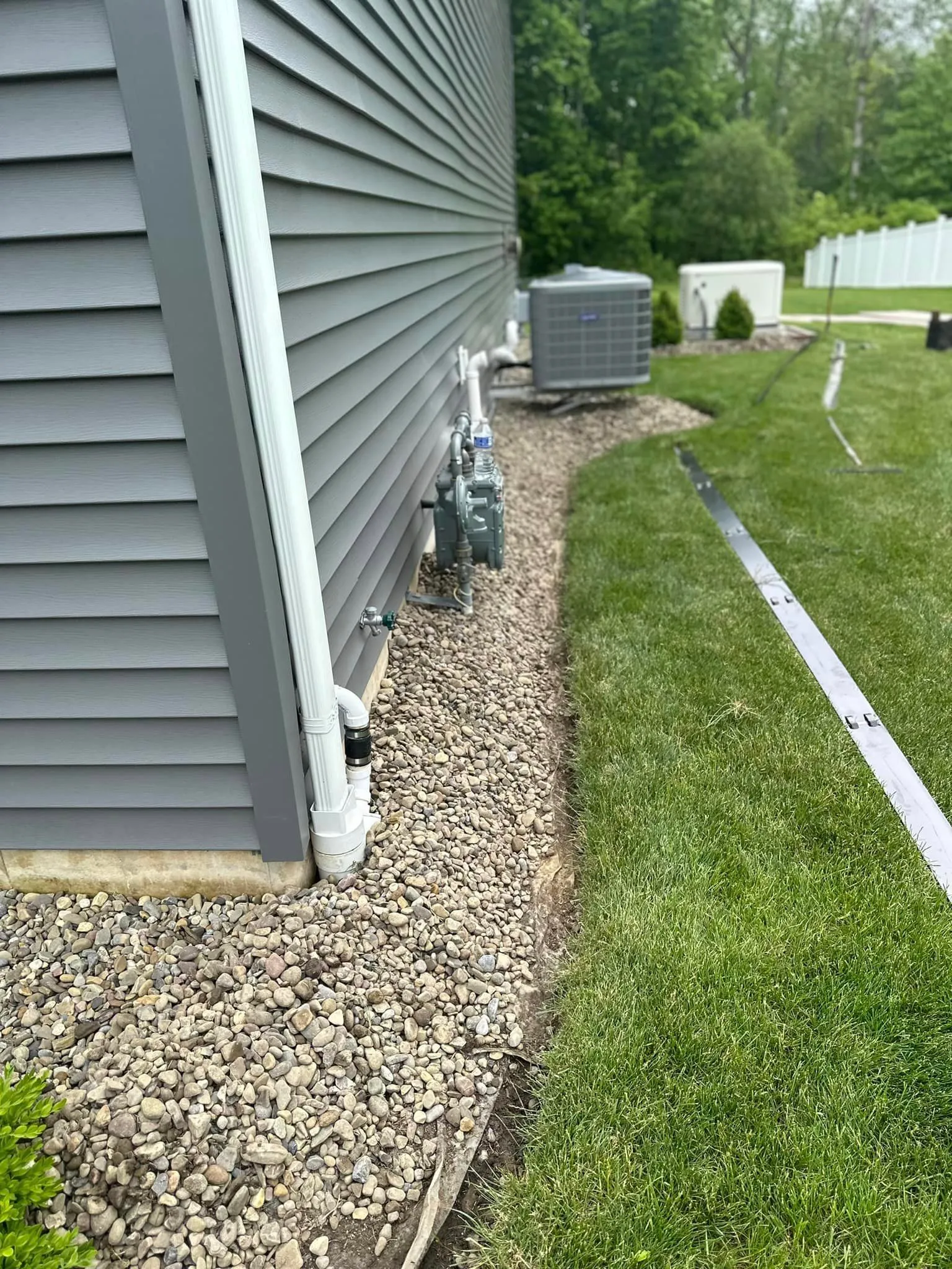 The side of a house with a strip of rocks along the foundation, bordered by a newly installed steel edge separating it from the grass lawn.