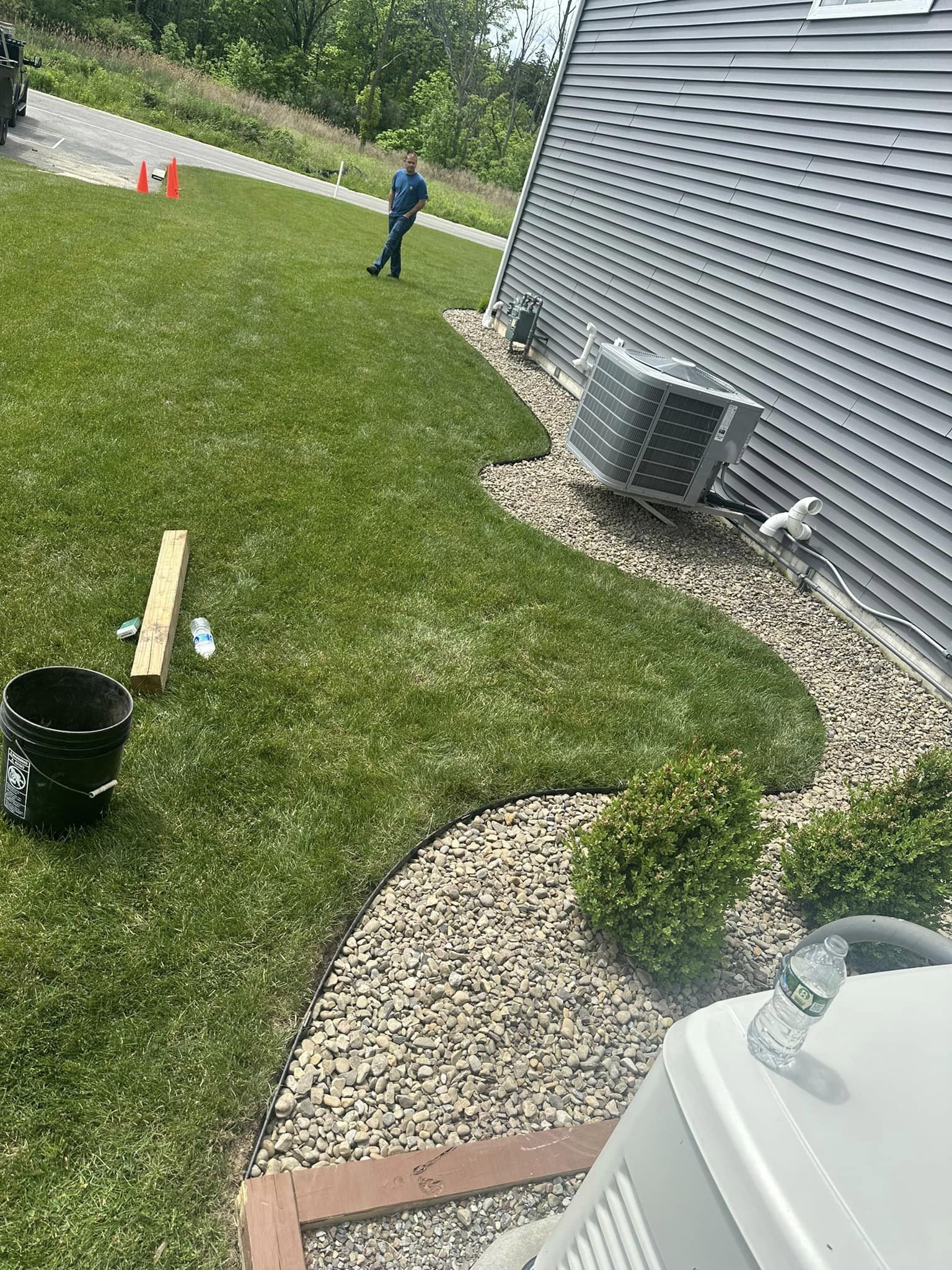 A landscaped garden bed with newly installed steel edging, rocks, and small shrubs, running along the side of a house. Grass lawn is neatly separated by the edging.