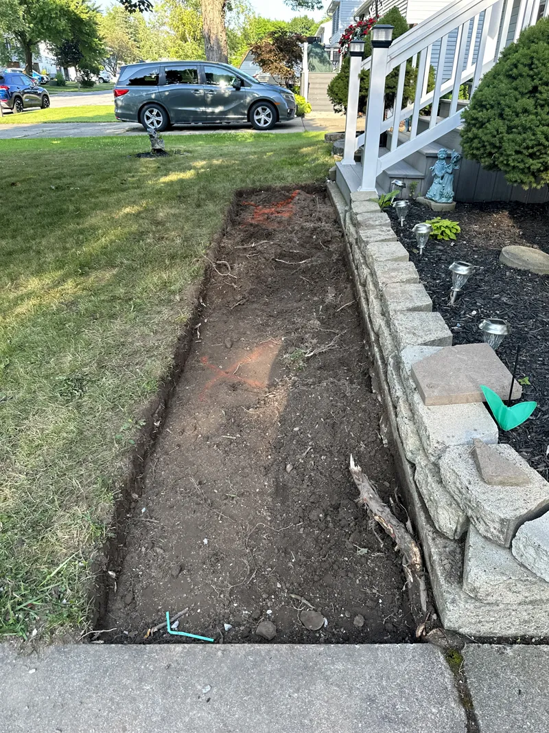 Excavated area prepared for the new brick pathway beside a garden bed.