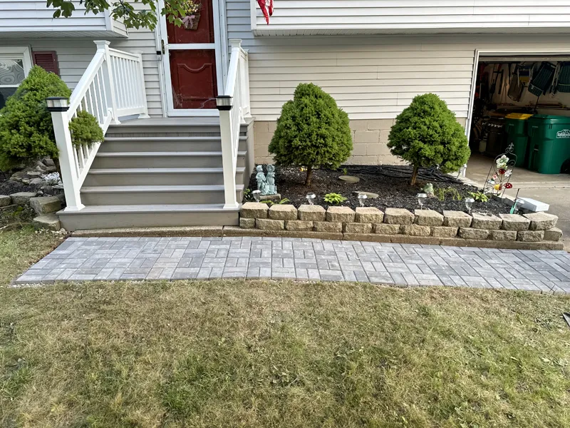 Completed brick pathway leading to front porch with white railings and decorative garden.