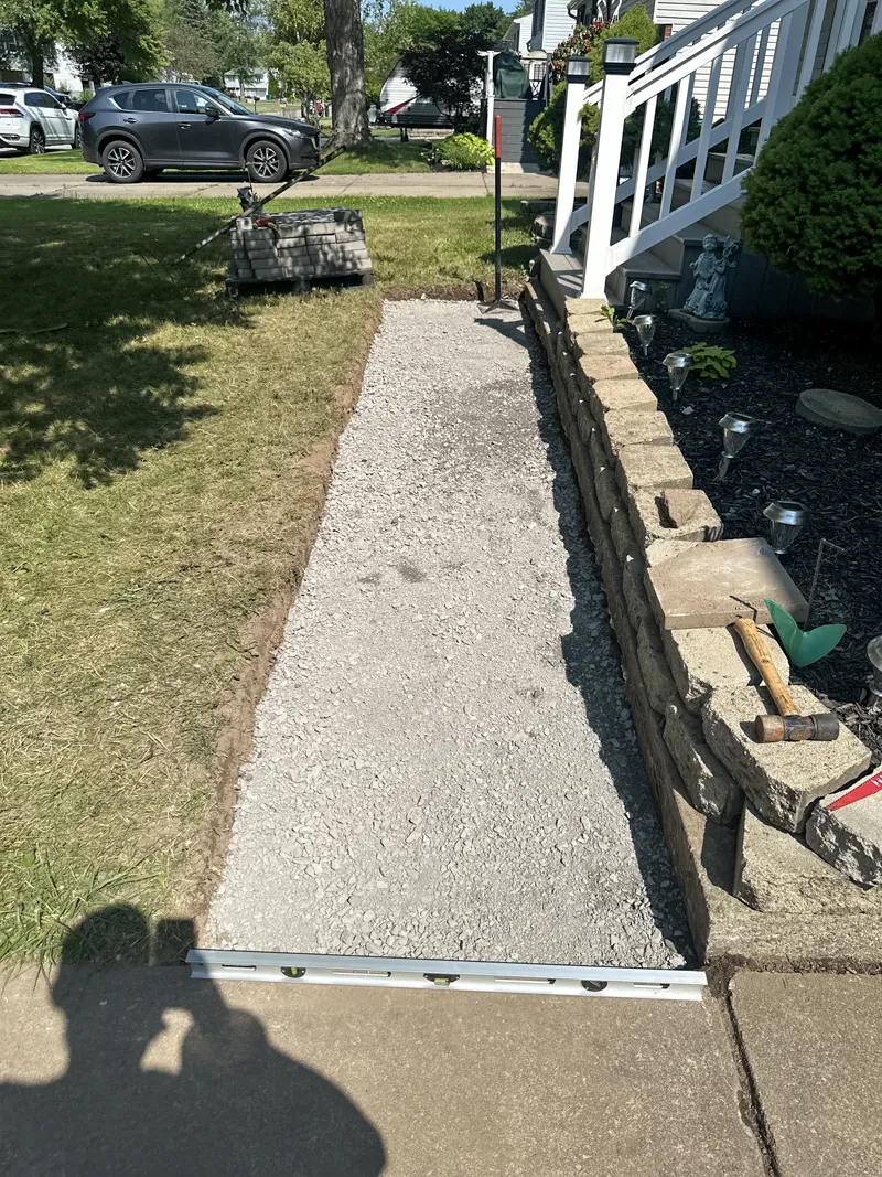 Partially completed brick pathway being laid next to a garden bed.