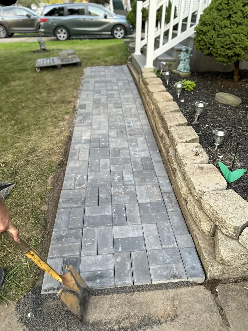 Worker smoothing the surface of the newly installed brick pathway with a tamper.