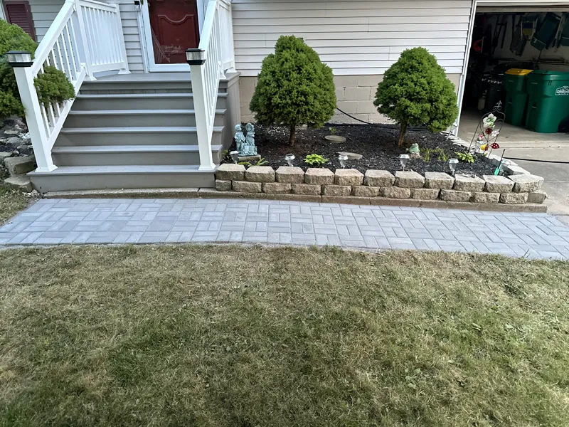 Overview of the completed brick pathway in front of a house, showing the front porch and garden.