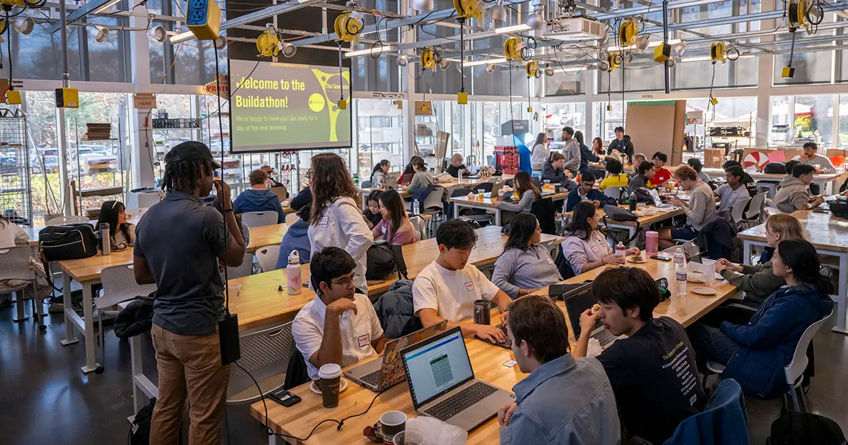 An interior wide shot of a large, modern workshop filled with a diverse group of young adults.