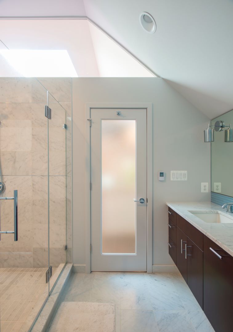 Luxurious attic bathroom transformation featuring marble surfaces, elegant fixtures, and ice blue glass tile accents in 1920s Crestwood home