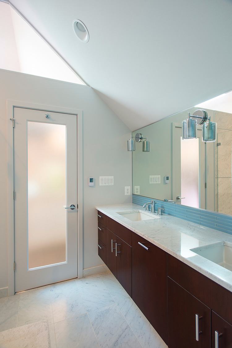 Shower enclosure featuring distinctive ice blue glass tile accents, rainfall showerhead, and premium fixtures
