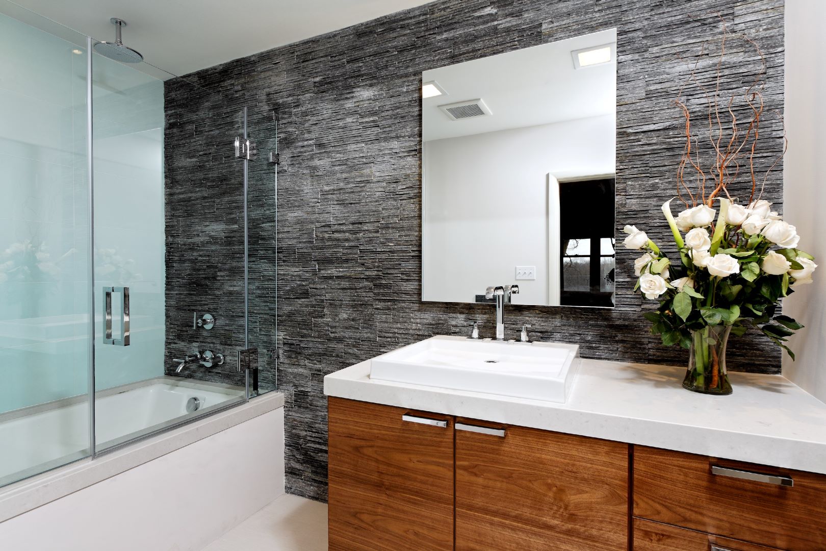 Detail of bathroom showing glass tile shower surround contrasting beautifully with natural stacked stone wall