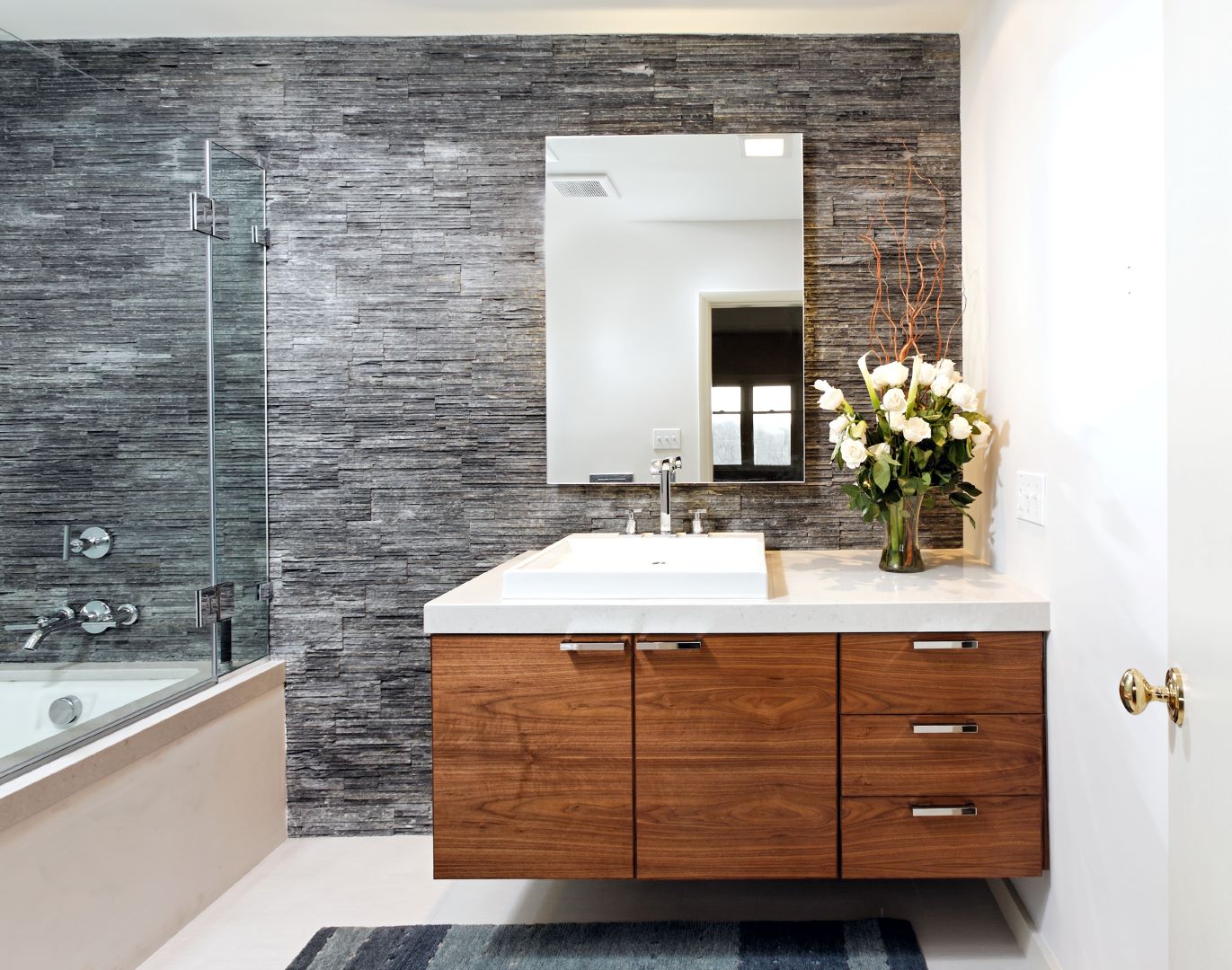 Luxurious guest bathroom featuring striking stacked stone accent wall, Porcelainosa tile flooring, and custom walnut vanity creating a spa-like retreat
