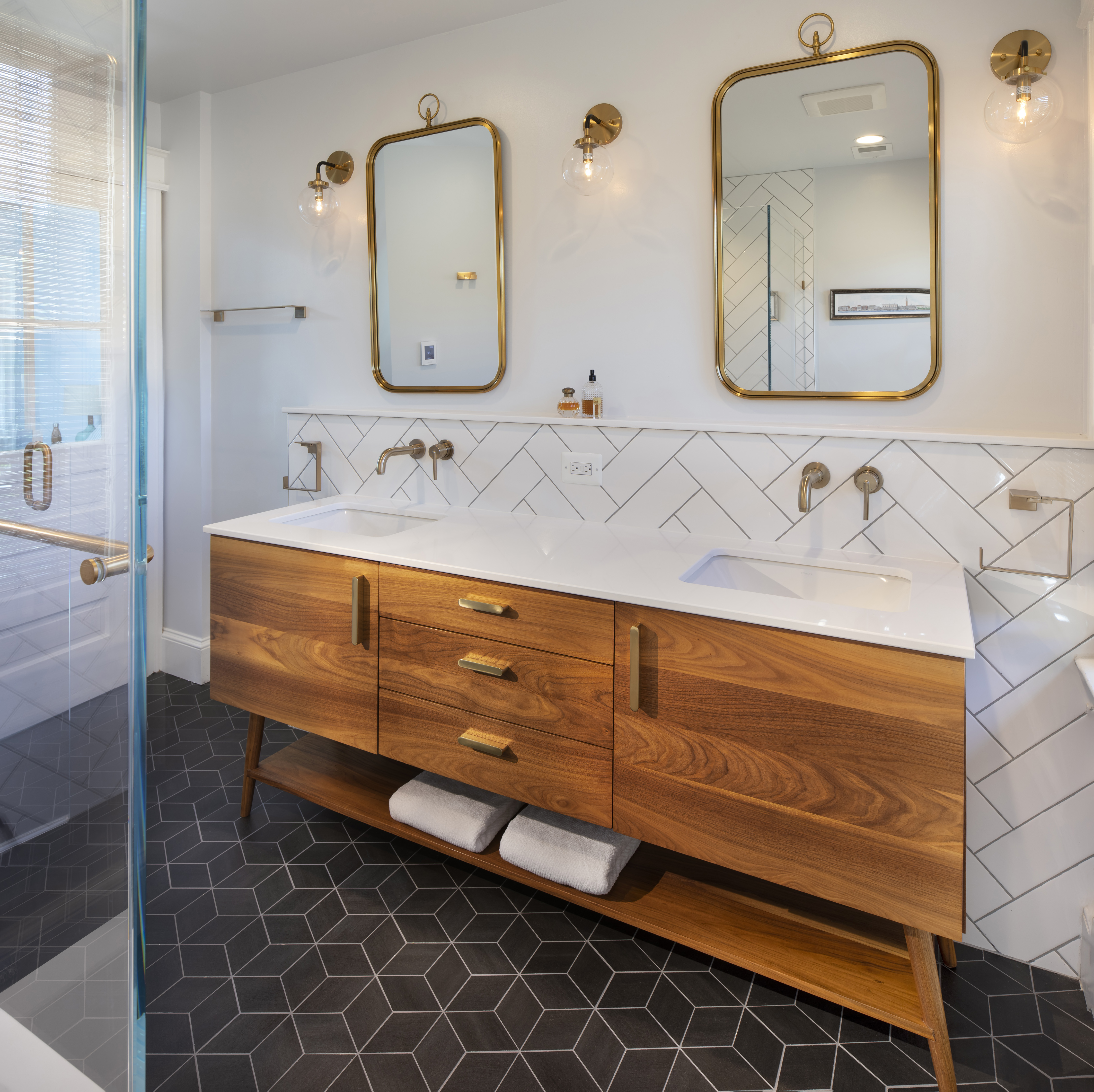 Detail of midcentury-inspired primary bath showing elegant gold fixtures, walnut vanity, and stylish towel arrangement