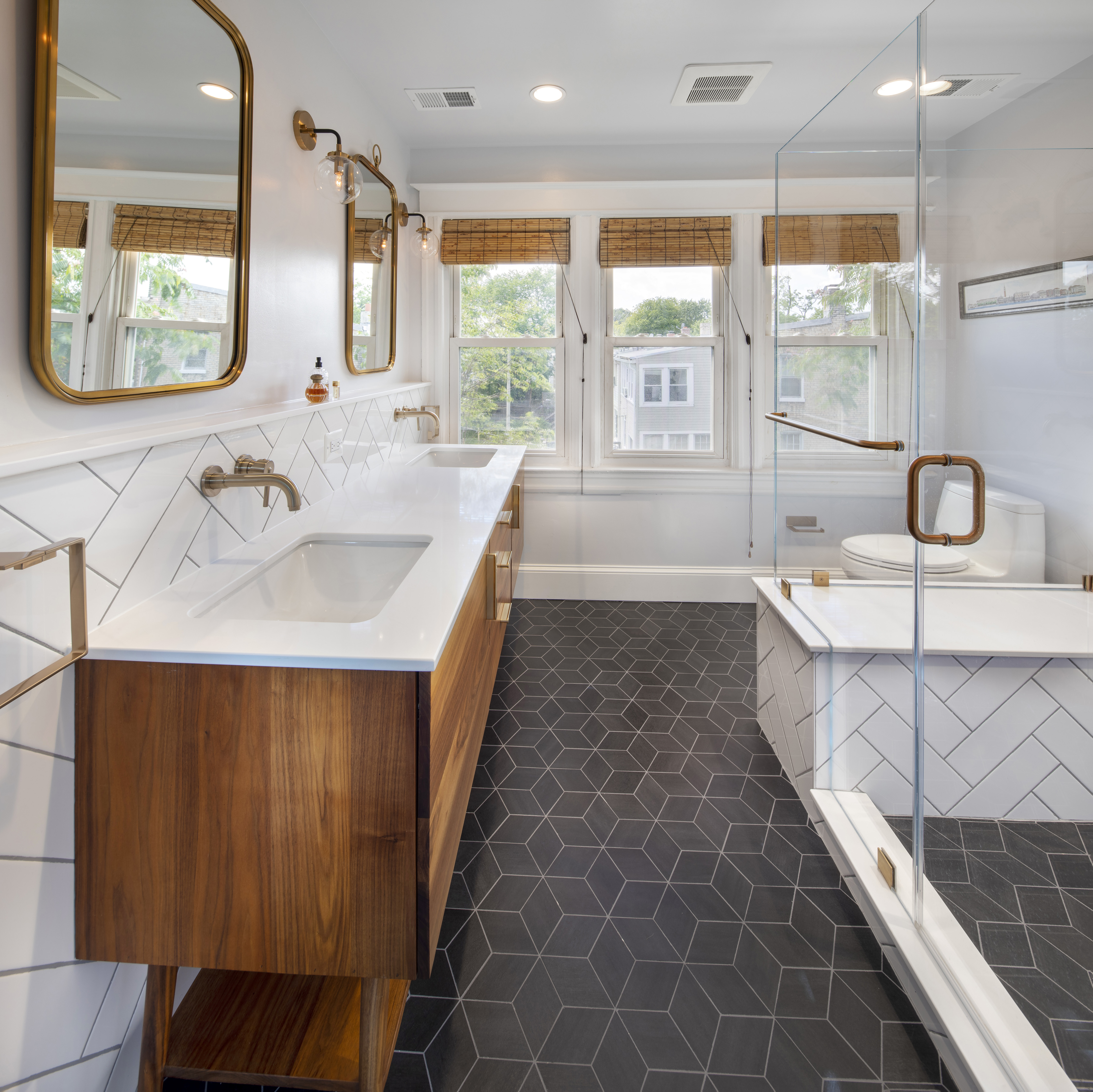 Panoramic view of primary bathroom featuring walnut midcentury double vanity, black and white tile, and gold accents