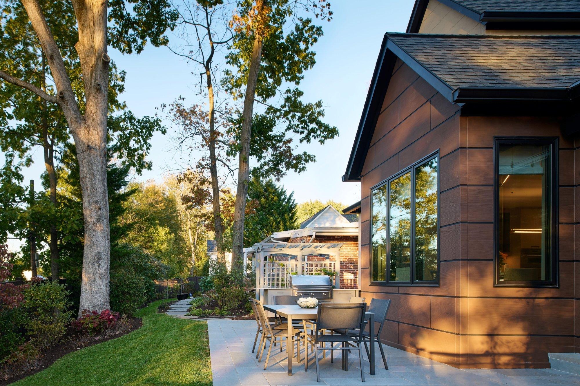 Stone patio and planted beds framed by mature trees beside a Landis addition