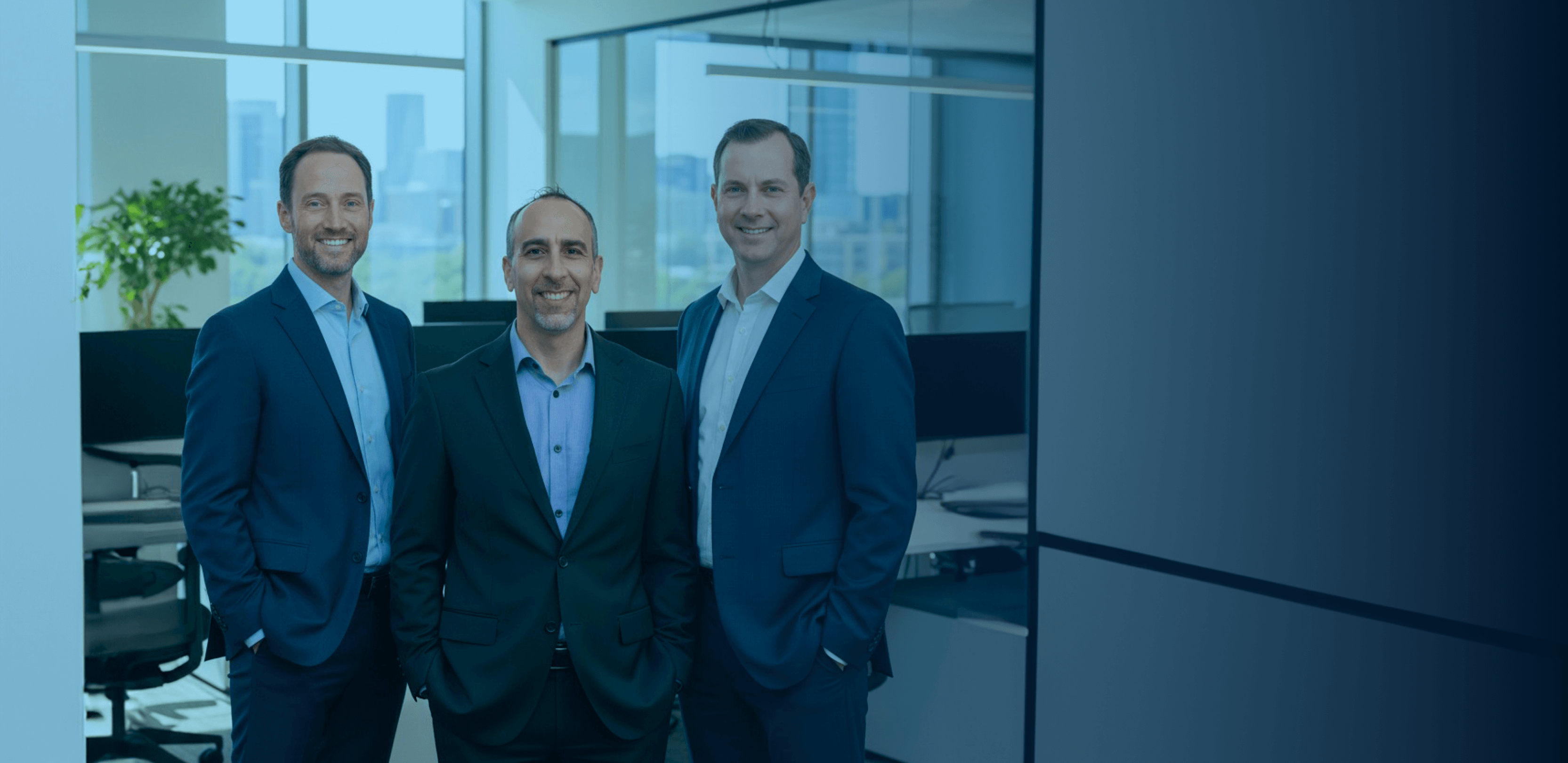 Two men in suits standing in a modern office with a city skyline visible through large windows.