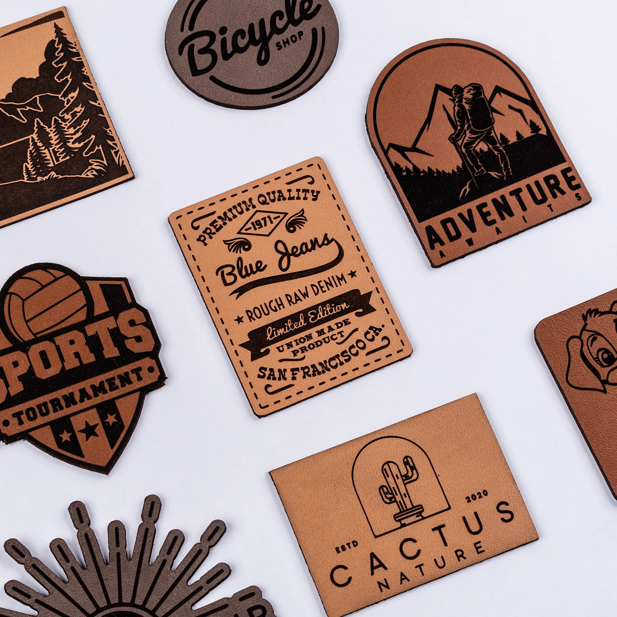 Assortment of brown leather patches with black designs and text including themes like sports, adventure, clothing brands, and a bicycle shop logo.