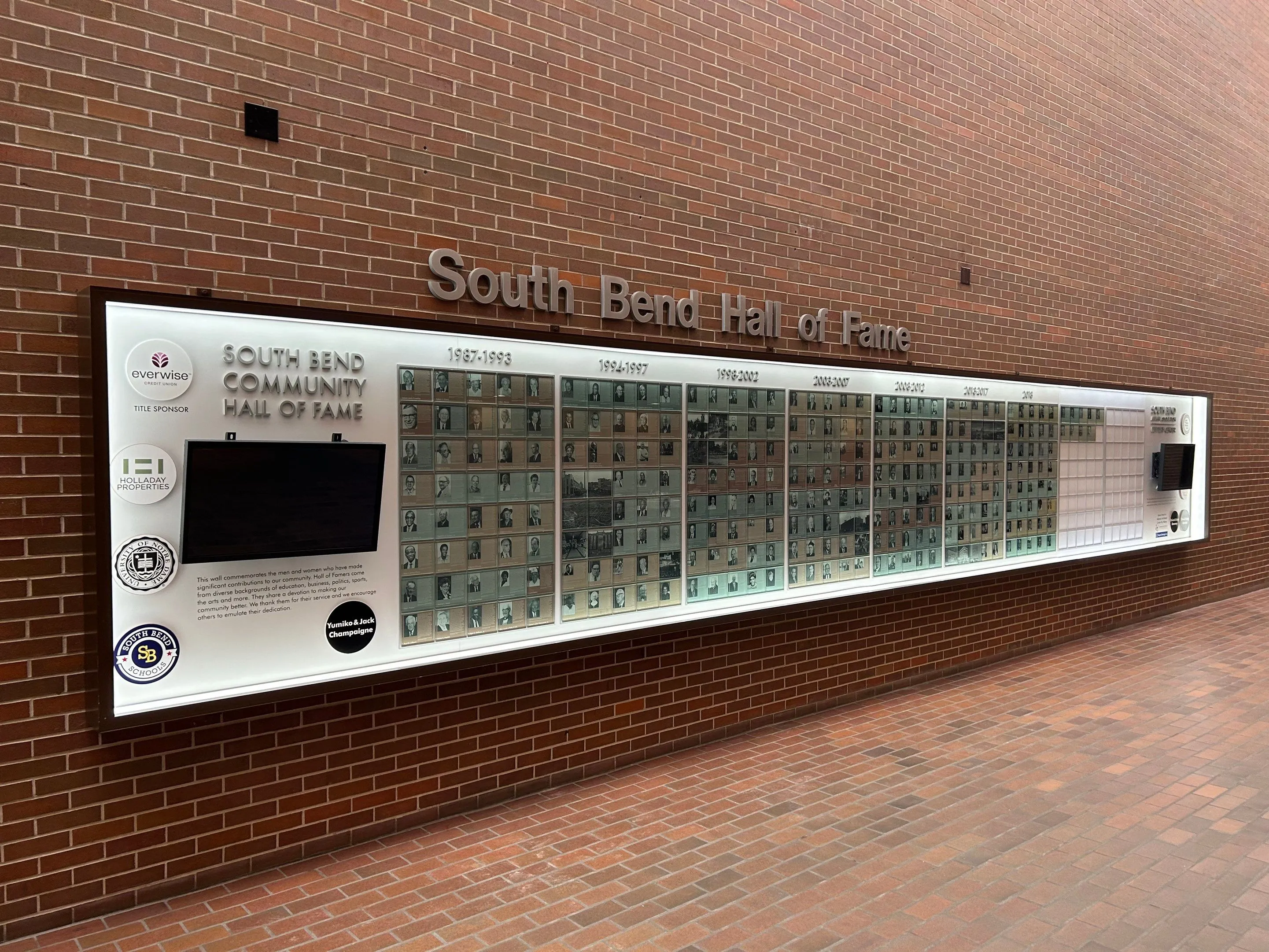 Long illuminated South Bend Community Hall of Fame wall display with photo plaques, sponsor logos, and an empty section for future honorees.