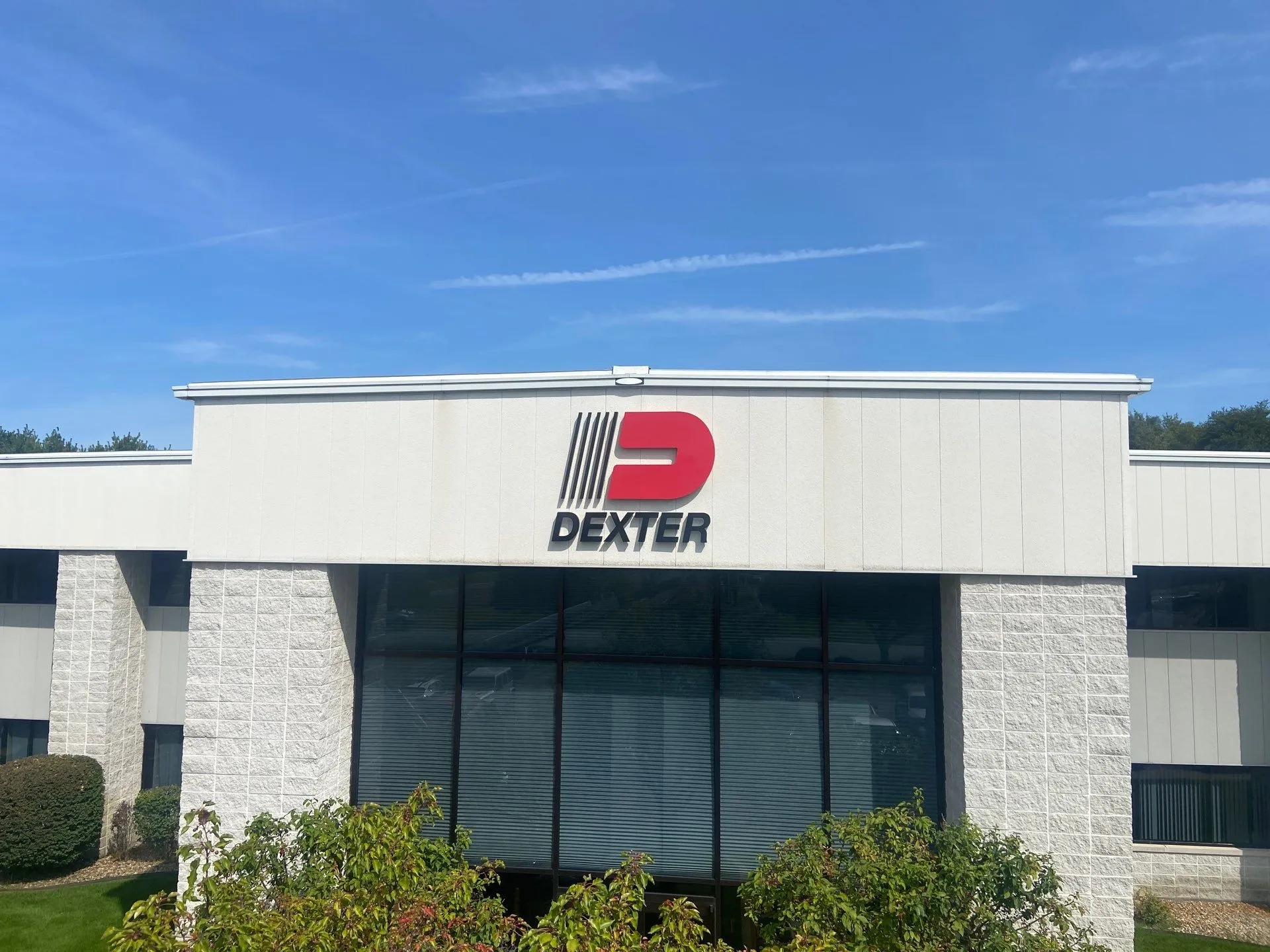 White commercial building with large windows and a red and black Dexter logo on the facade under a blue sky.