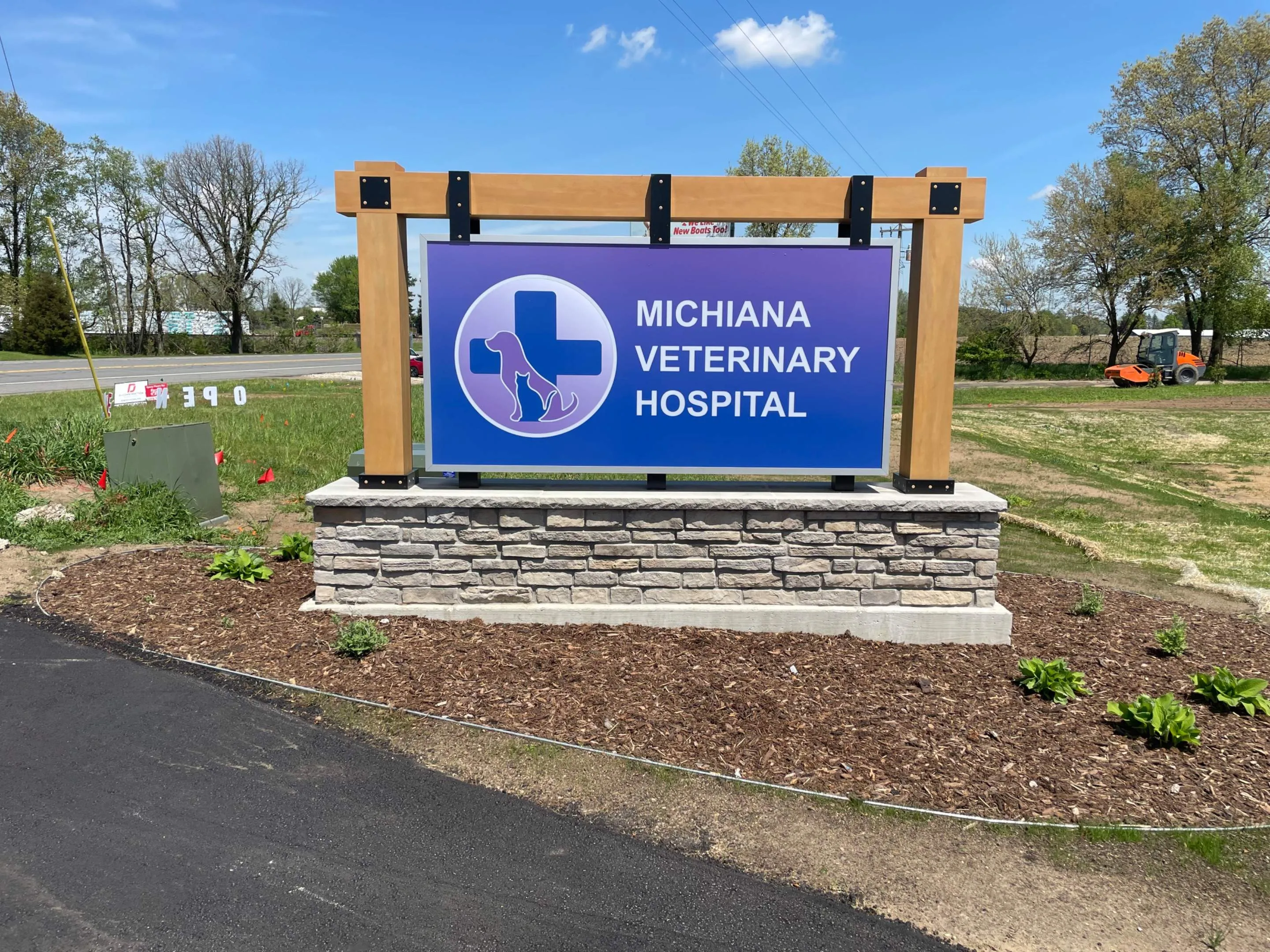 Outdoor sign for Michiana Veterinary Hospital mounted on stone and wood frame with a blue background featuring a dog and cat silhouette inside a medical cross.