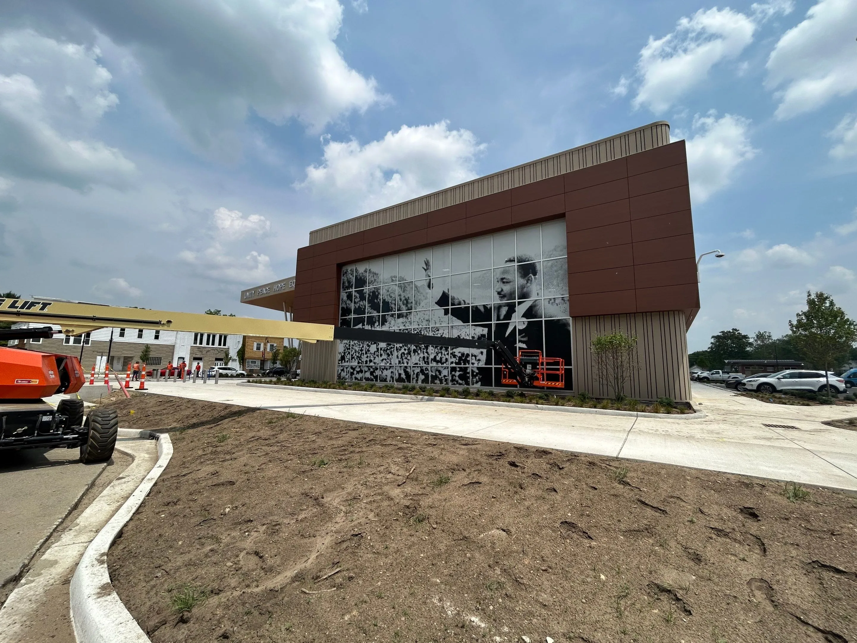 Modern building with large black-and-white mural of Martin Luther King Jr. waving, with construction lift and workers nearby.