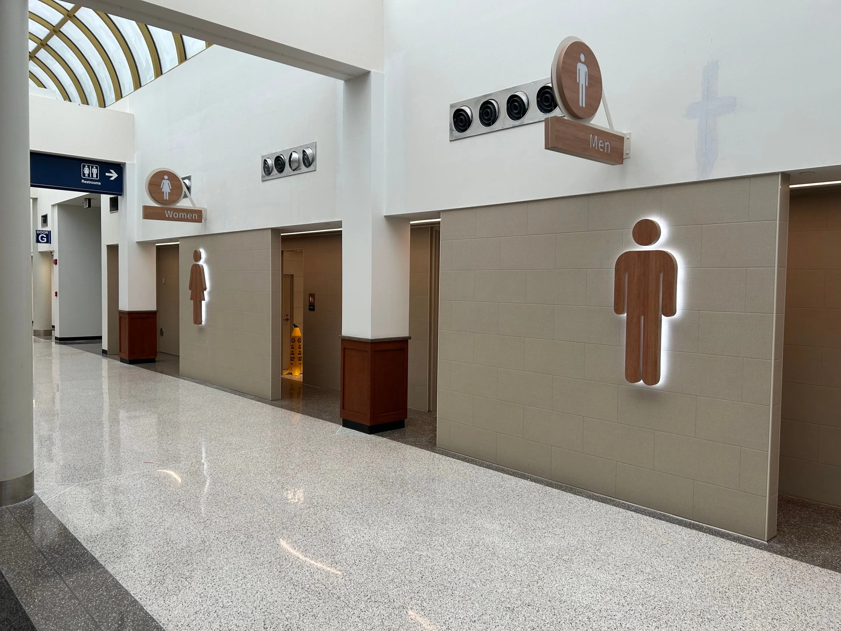 Corridor with entrances to men's and women's restrooms marked by wooden illuminated figures and signs.
