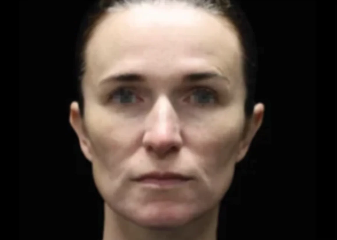 Close-up front view of a serious woman with slicked-back hair against a black background.