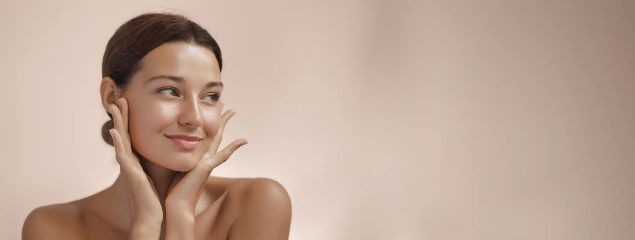 Smiling woman with clear skin gently touching her face against a soft beige background.