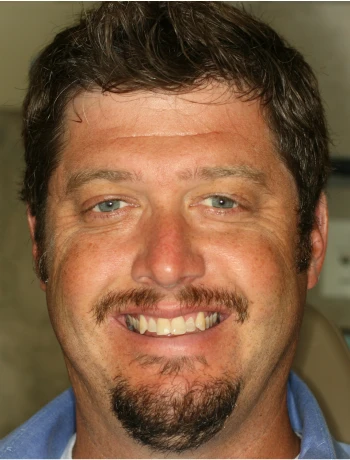 Smiling man with short brown hair, blue eyes, a mustache, and a goatee wearing a blue shirt.