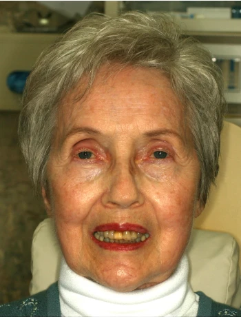 Close-up portrait of an elderly woman with short gray hair, wearing a white turtleneck and dark sweater, smiling.